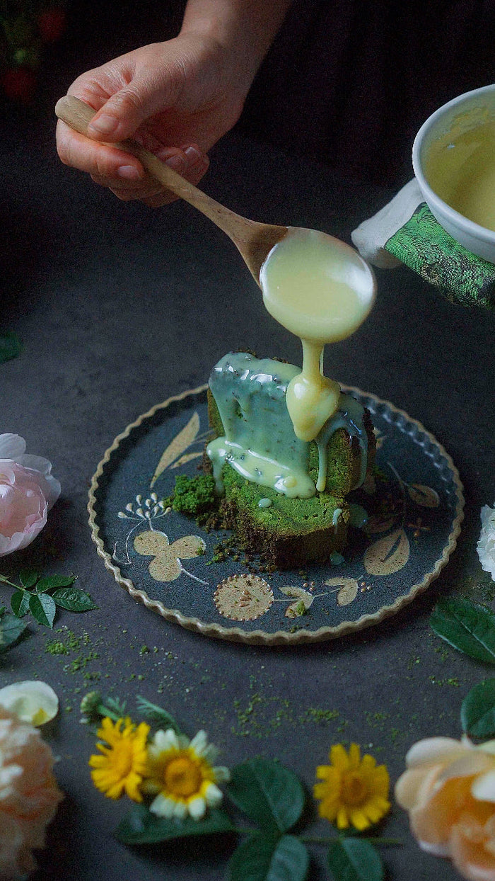 Pouring glaze over a slice of keto matcha pound cake recipe on a decorative plate surrounded by flowers